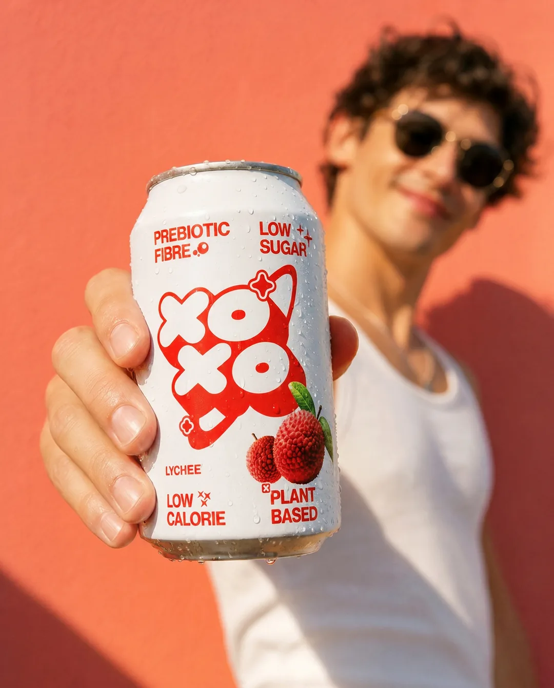 Man in sunglasses holding out a lychee can against a coral wall