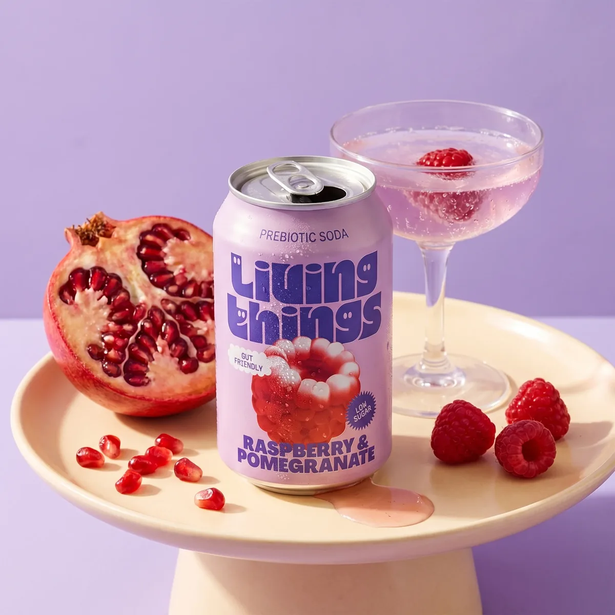 A single soft drink can presented on a cake stand with fresh pomegranate, styled as a premium retail hero